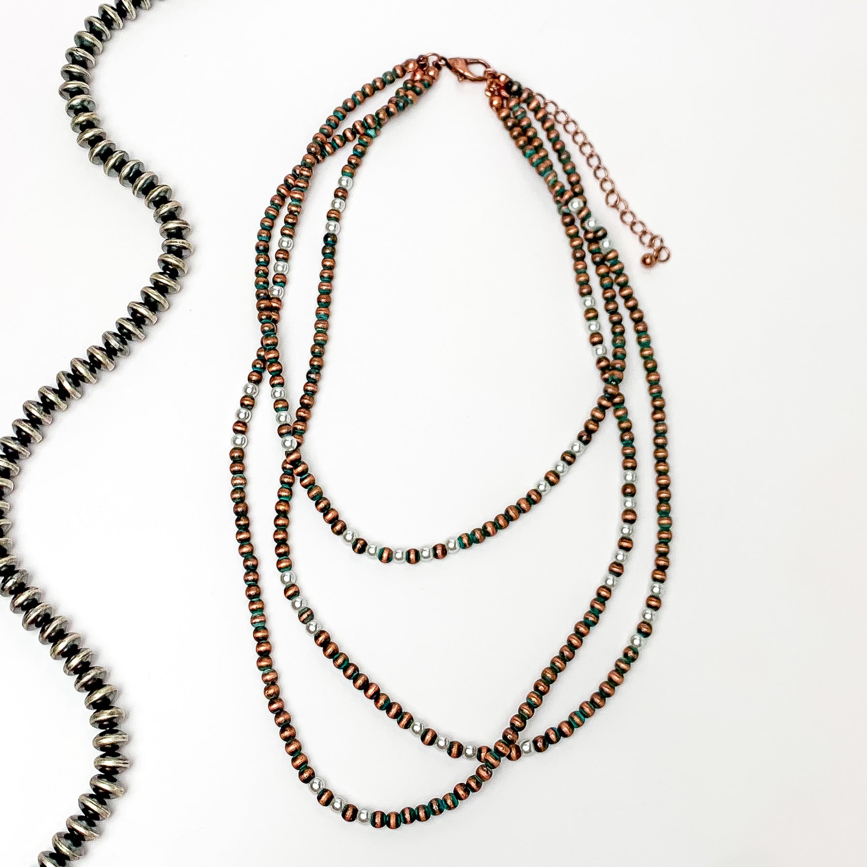There stands of patina faux navajo pearls with white pearls as well. Pictures on a white background with a strand of silver beads to the left.
