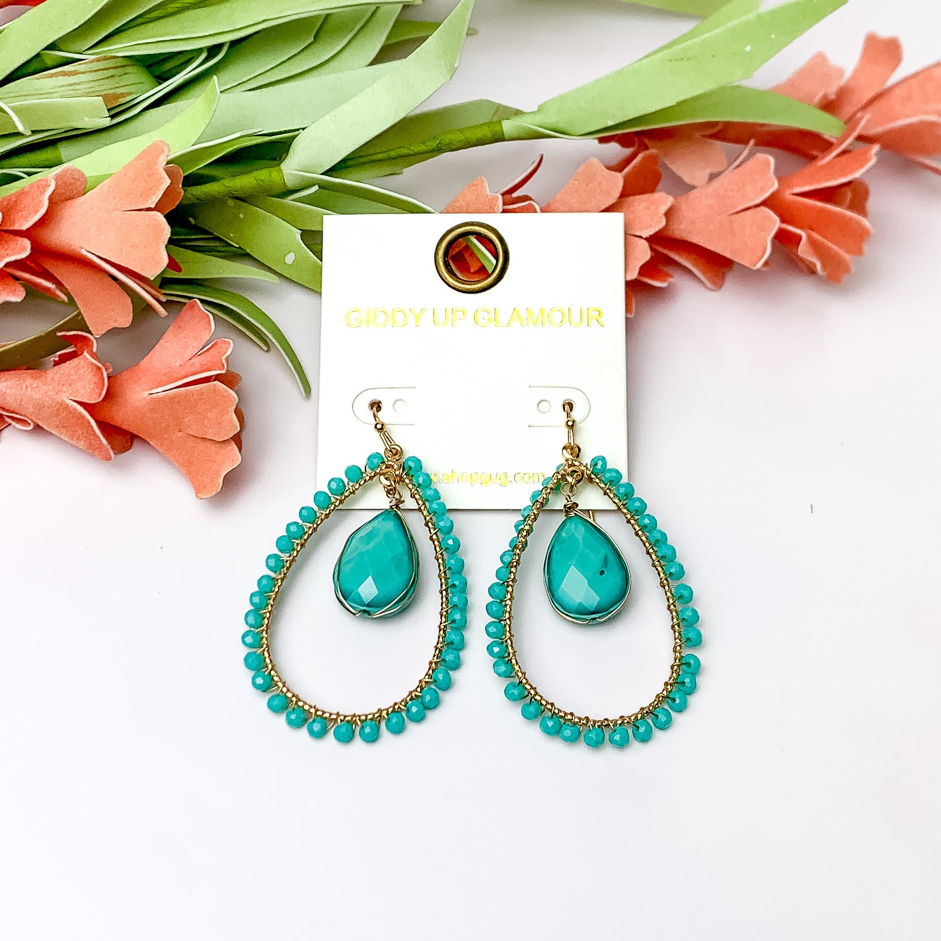 Turquoise Stone Inside Open Beaded Teardrop Earrings with Gold Tone Outline. Pictured on a white background with flowers at the top.