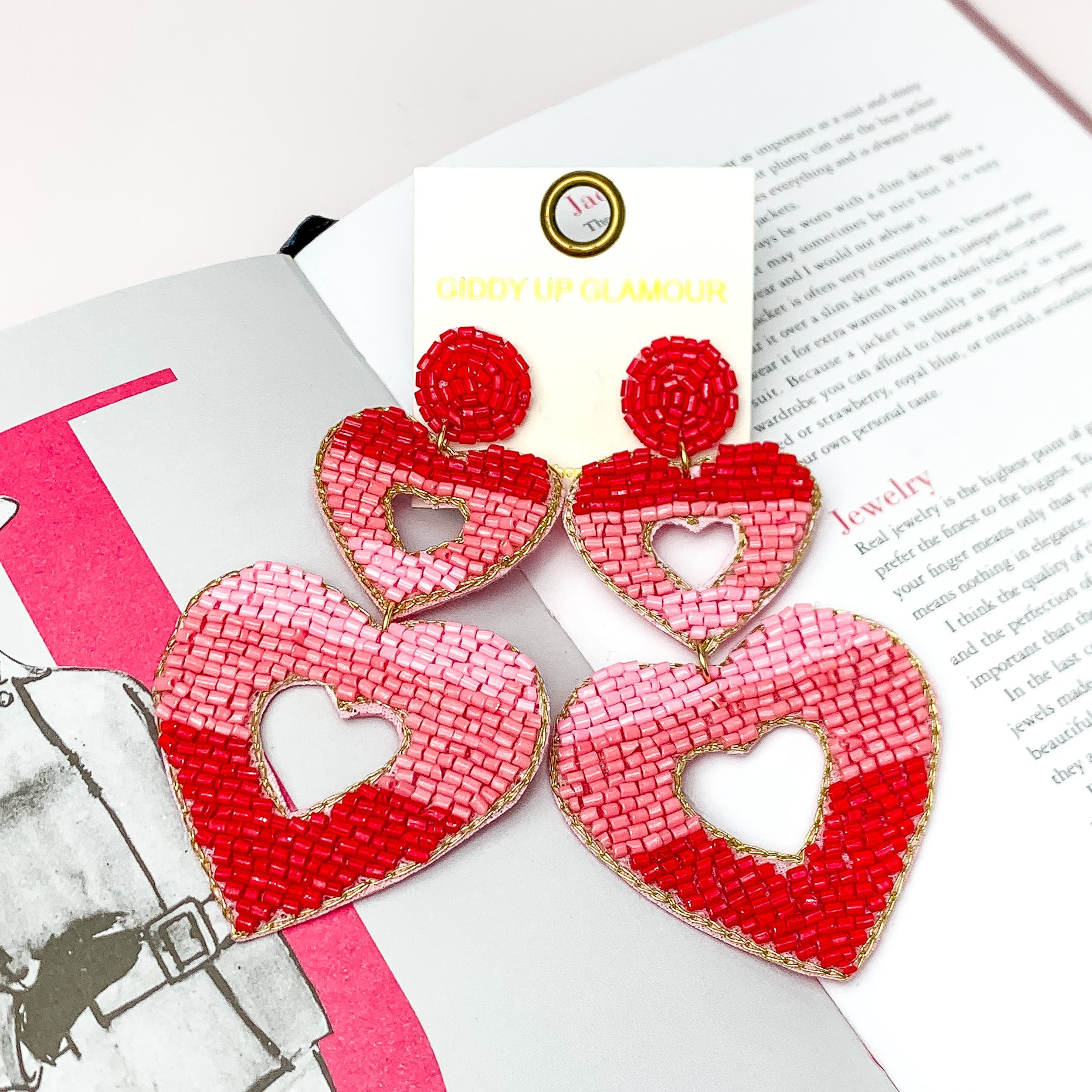Beaded Two Tier Open Heart Earrings in Red, and Pink. Pictured on a white background with a book behind the earrings.