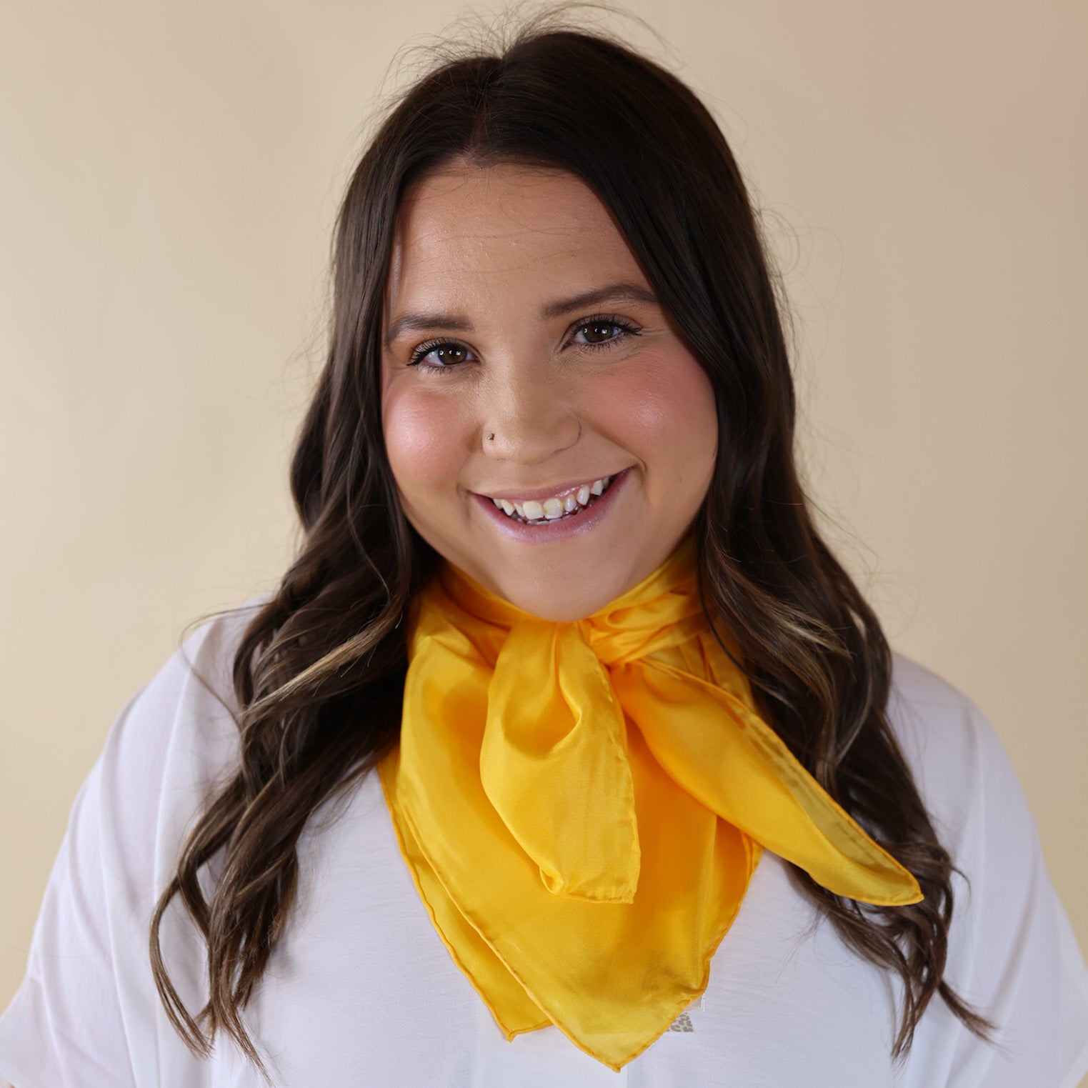 Brunette model wearing a white, drop shoulder top with solid yellow scarf tied around her neck. Model is pictured in front of a beige background.