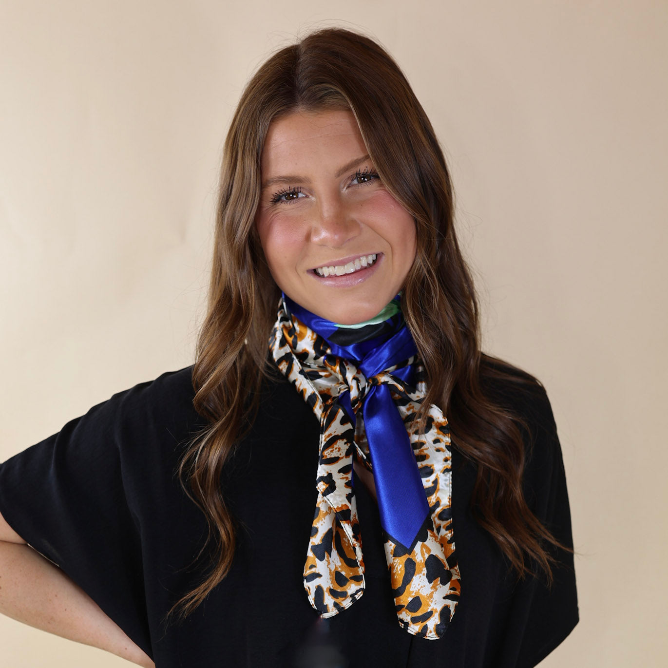 Brunette model wearing a black, drop shoulder top with royal blue and leopard outline scarf with tied around her neck. Model is pictured in front of a beige background. 
