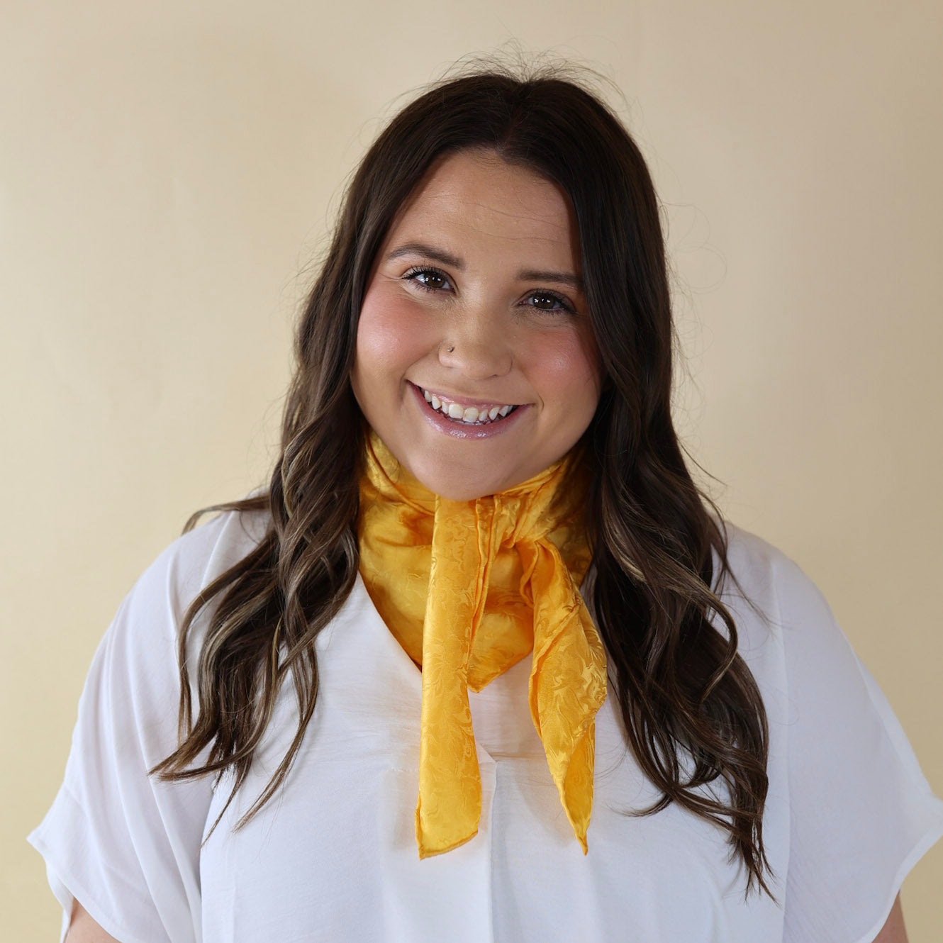 Brunette model wearing a white, drop shoulder top with a yellow jacquard print scarf tied around her neck. Model is pictured in front of a beige background. 
