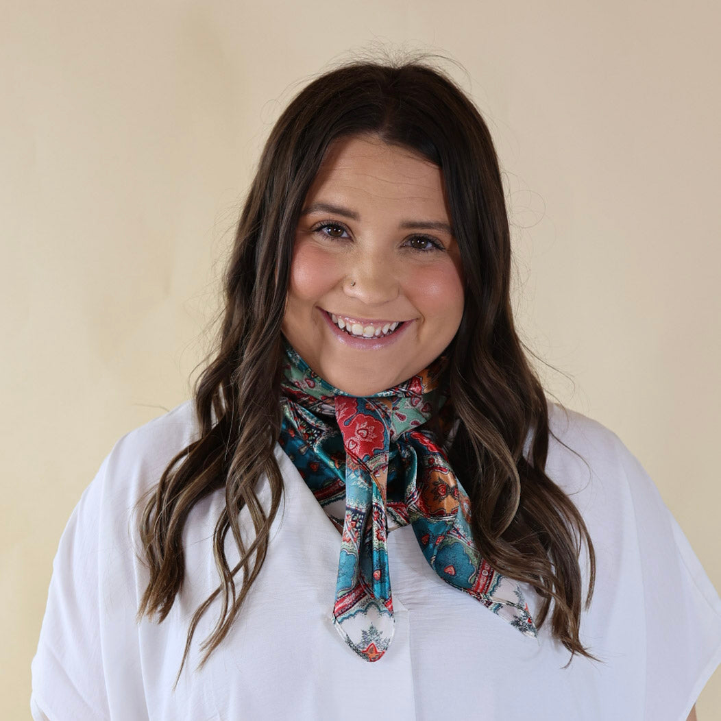 Brunette model wearing a white, drop shoulder top with multicolored paisly print scarf with tied around her neck. Model is pictured in front of a beige background. 