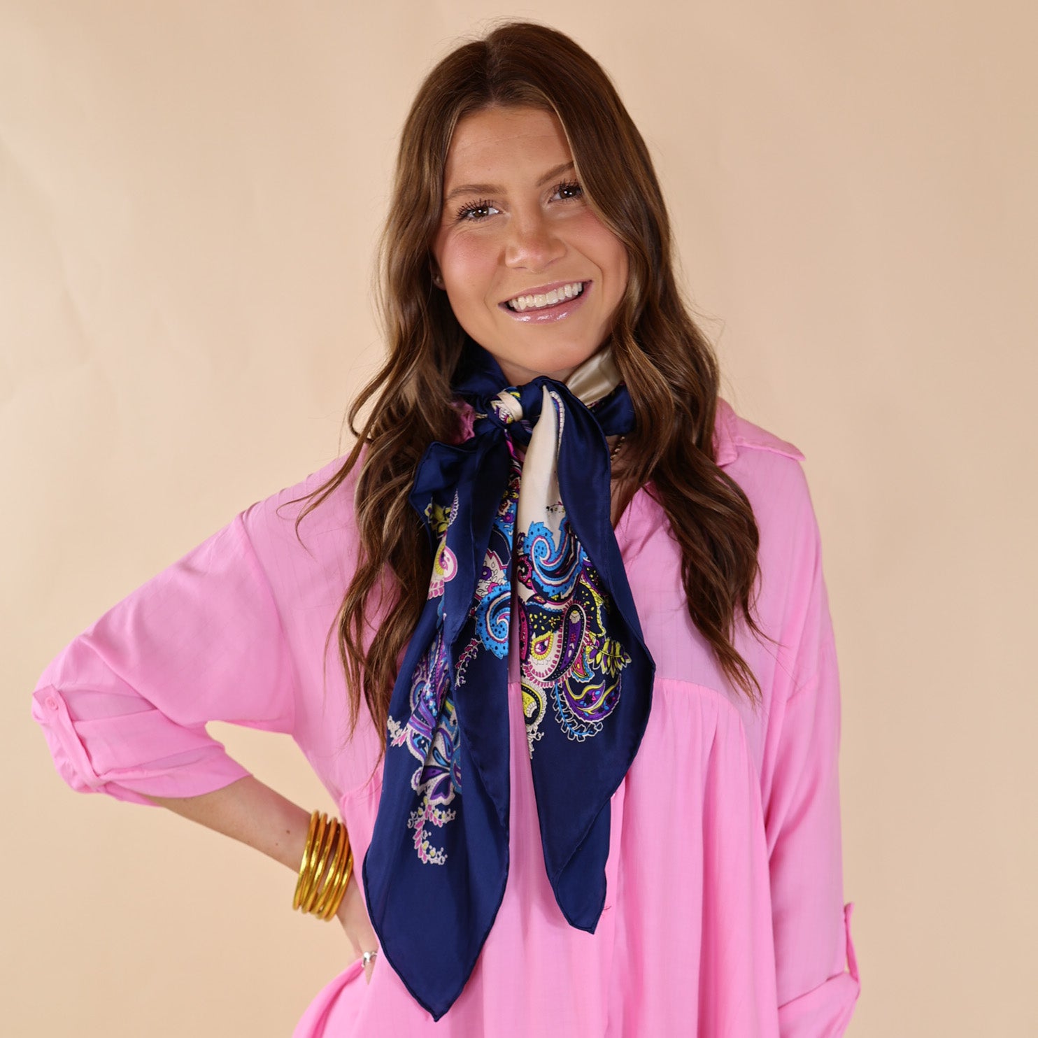 Brunette model wearing a Pink, drop shoulder top with Multicolored scarf tied around her neck. Model is pictured in front of a beige background.