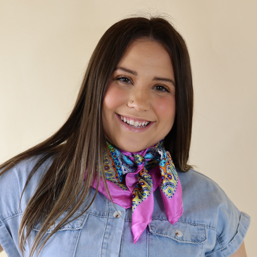 Brunette model wearing a white, drop shoulder top with multicolored print scarf with tied around her neck. Model is pictured in front of a beige background.