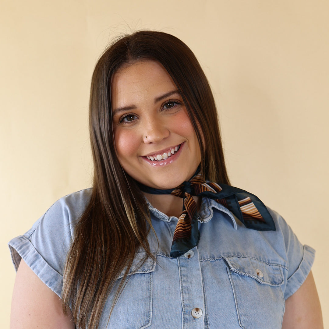 Brunette model is pictured wearing an ivory, leopard print long sleeve top and a blue and brown striped scarf tied around her neck. She is pictured in front of a beige background. 