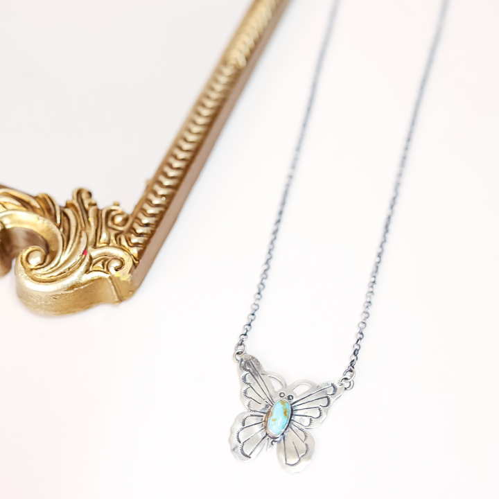 Butterfly-shaped pendant on a chain with a gold and silver design element.