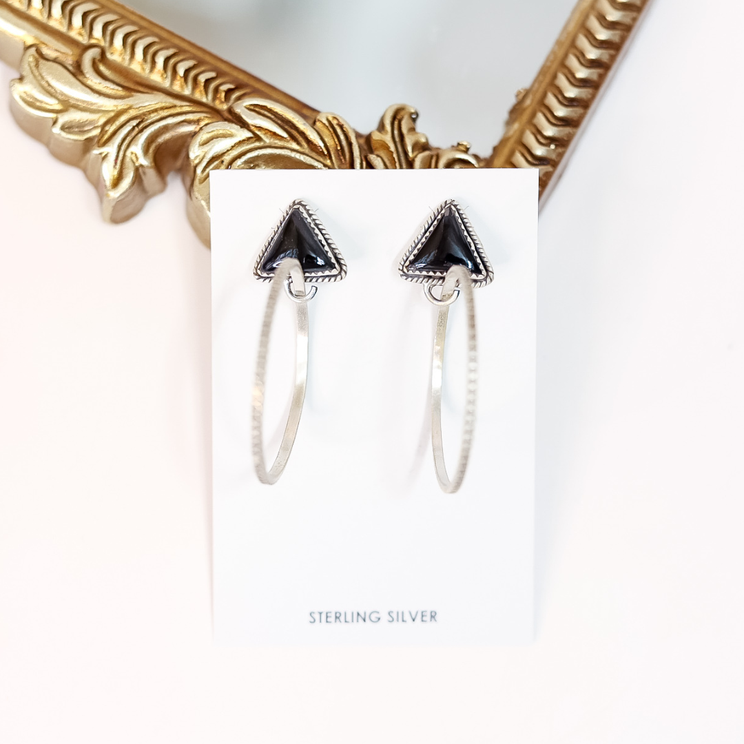Pair of silver hoop earrings with black triangle accents on a white card, with a gold frame in the background.