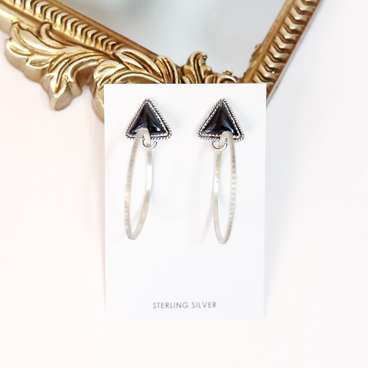 Pair of silver hoop earrings with black triangle accents on a white card, with a gold frame in the background.