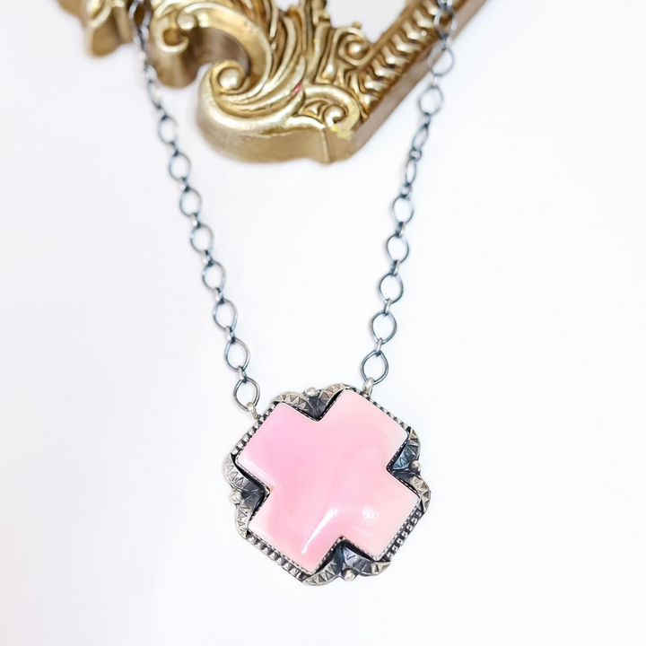 Sterling silver necklace with pink conch shell cross pendant handcrafted by Native American artist Tia Long, displayed on white background with ornate gold frame.
