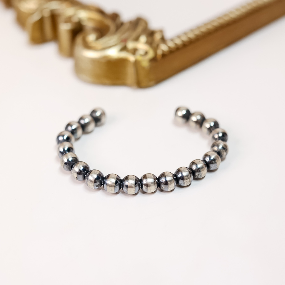 Adjustable sterling silver cuff bracelet with 8mm oxidized Navajo pearls, styled against a gold mirror frame background.