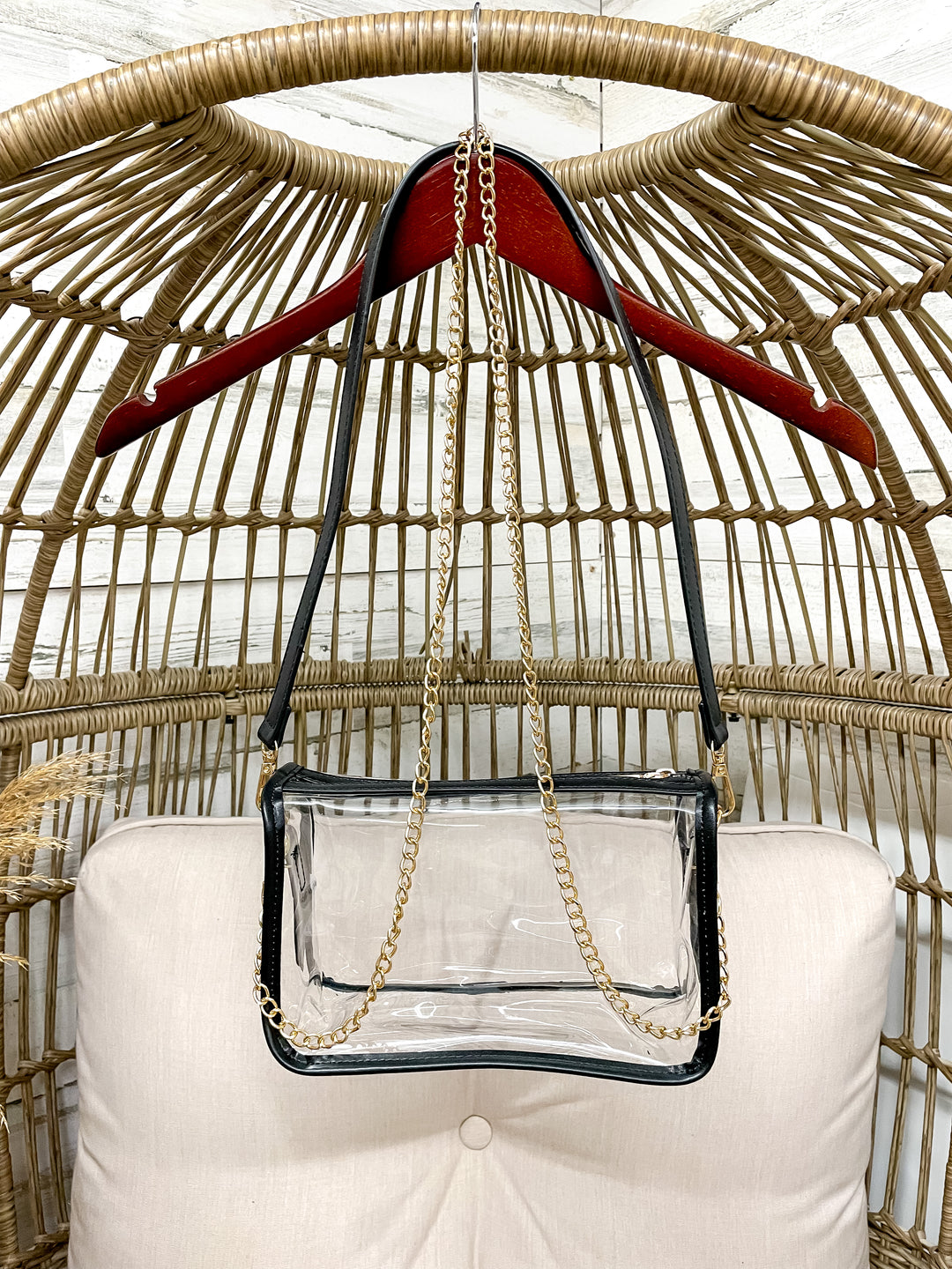 Clear handbag with a gold chain on a red hanger against a wicker chair background