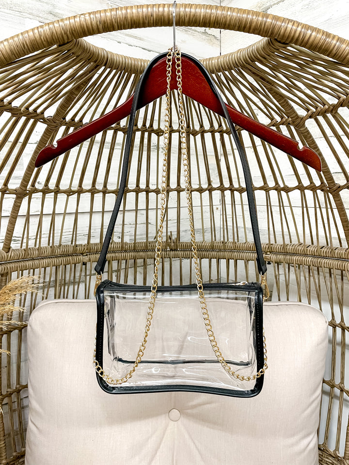 Clear handbag with a gold chain on a red hanger against a wicker chair background