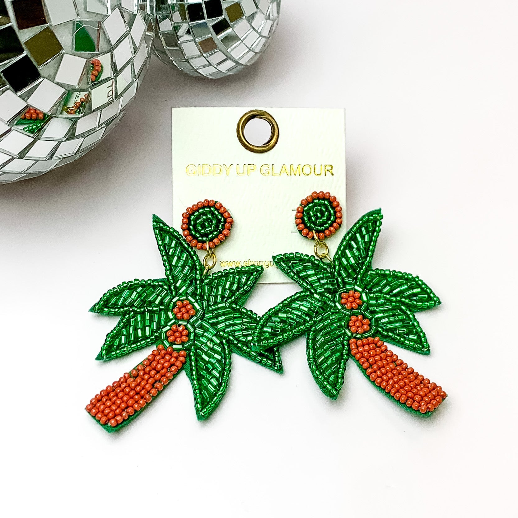 Bright green beaded palm tree earrings. Pictured on a white background with disco balls in the top left corner.