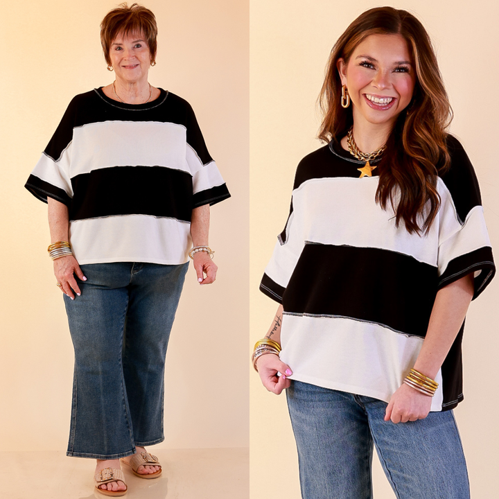 Models are wearing Color Block Rugby Style Wide Stripe Relaxed Short Sleeve Top in Black with Jeans against a beige backdrop. 