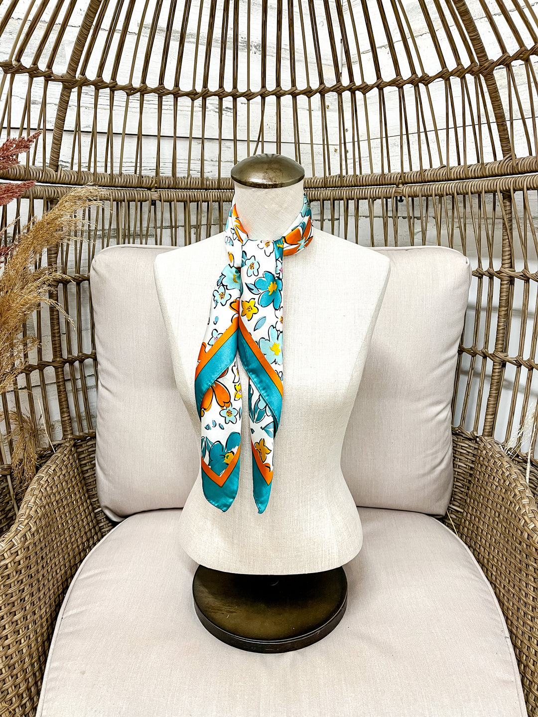 Mannequin with a colorful scarf draped over it, sitting on a wicker chair with a white cushion.