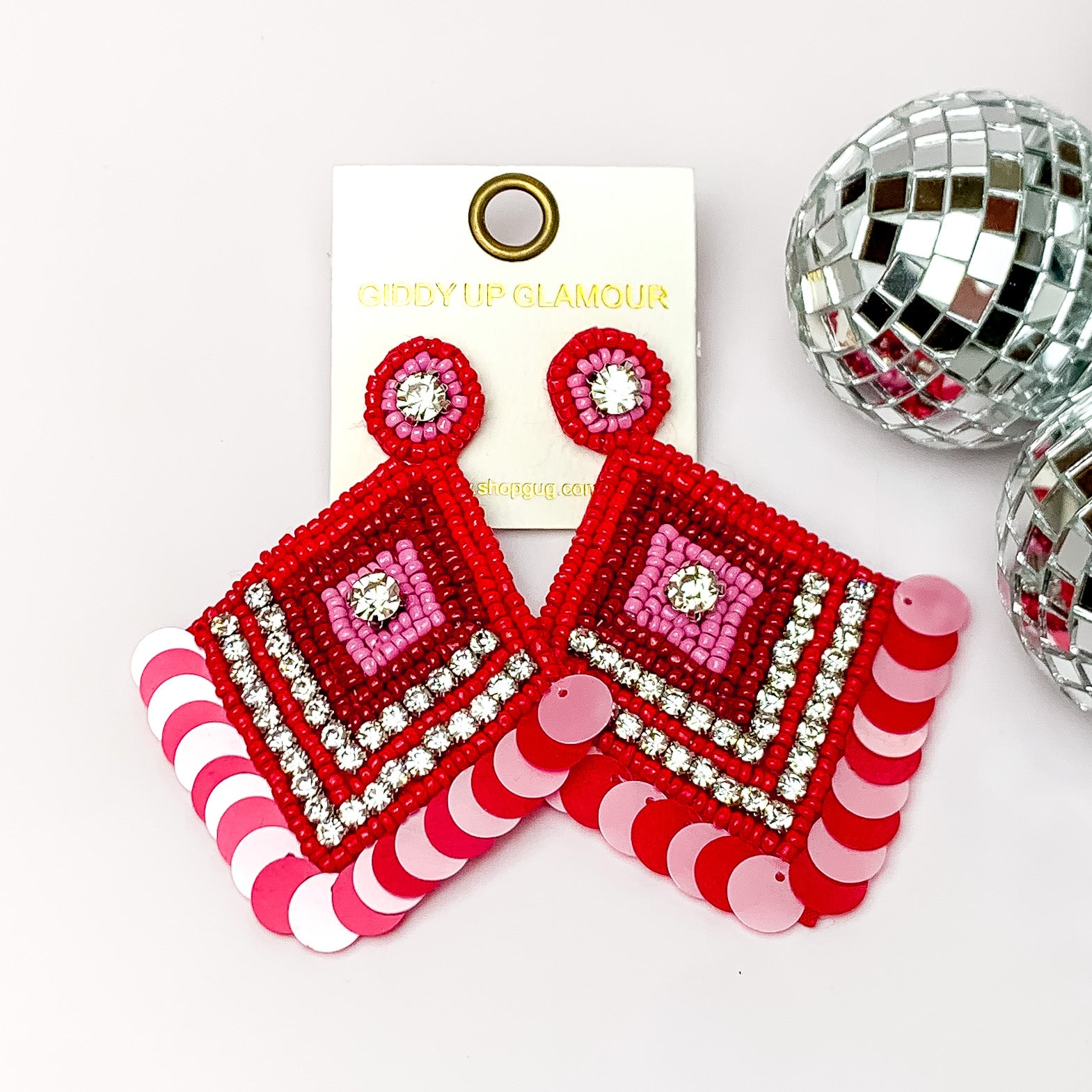 Fashionista Diamond Shaped Beaded Earrings in Red, and Lavender. Pictured on a white background with disco balls on the right side.