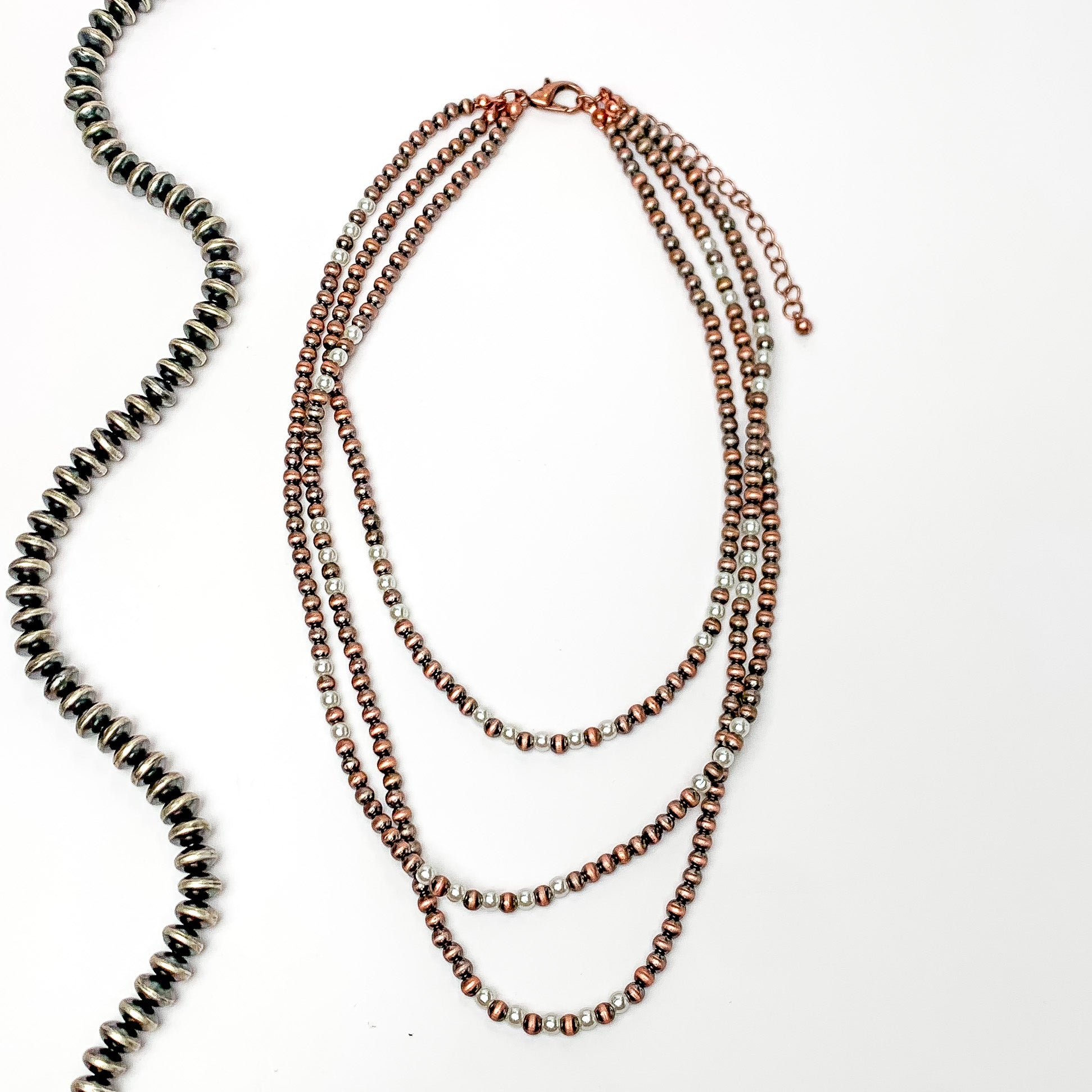 There stands of copper faux navajo pearls with white pearls as well. Pictures on a white background with a strand of silver beads to the left.