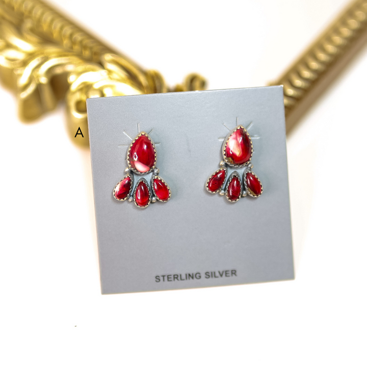 Red earrings on a silver card with 'Sterling Silver' text, gold necklace in the background