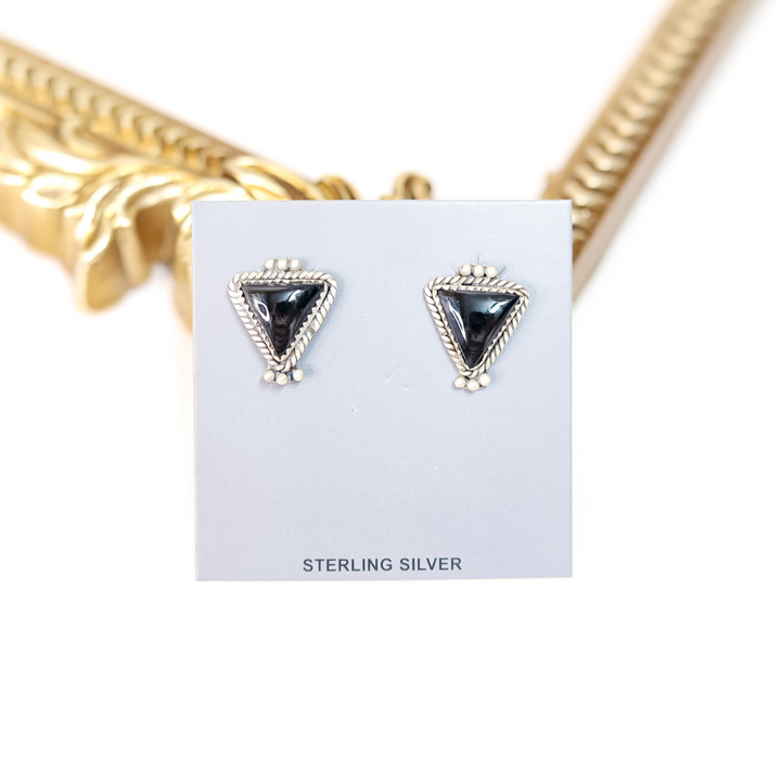 A pair of sterling silver triangle stud earrings featuring black onyx stones, displayed on a gray card with “STERLING SILVER” printed at the bottom.