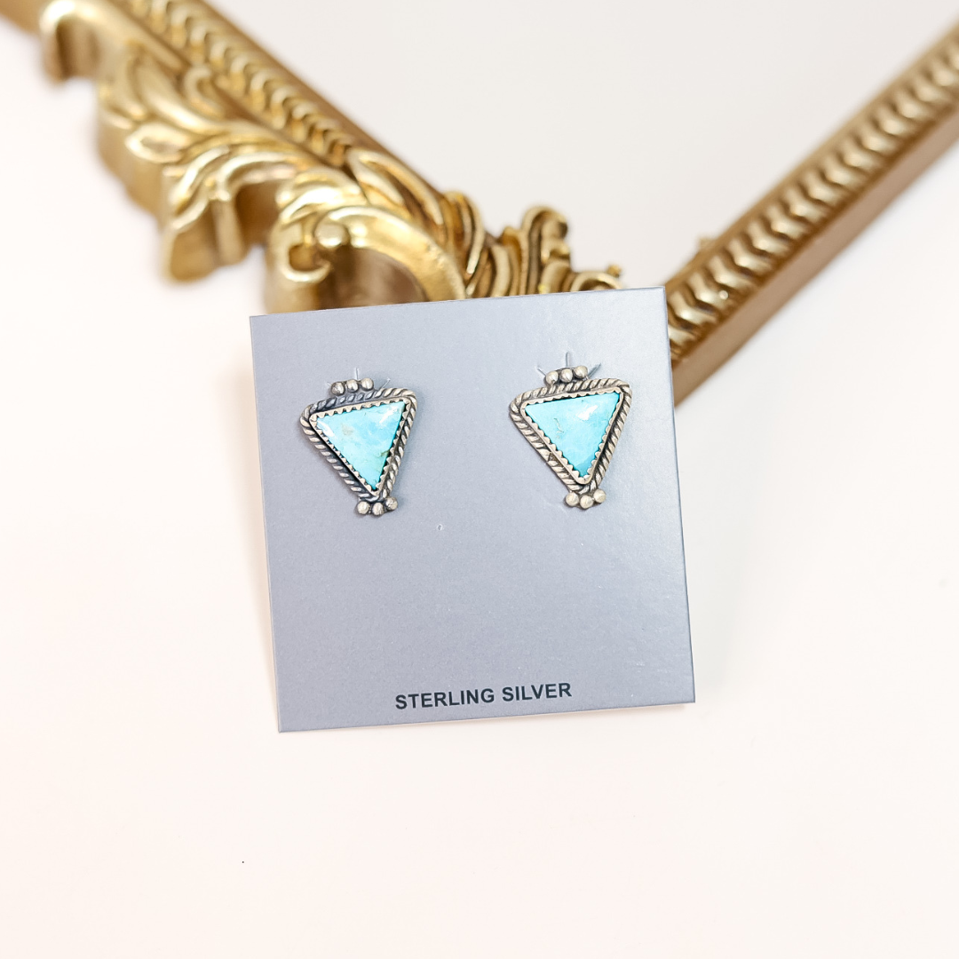 Sterling silver triangle-shaped earrings on a card with gold decorative frame in the background