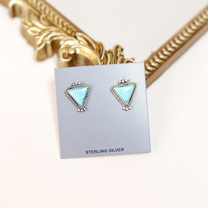 Sterling silver triangle-shaped earrings on a card with gold decorative frame in the background