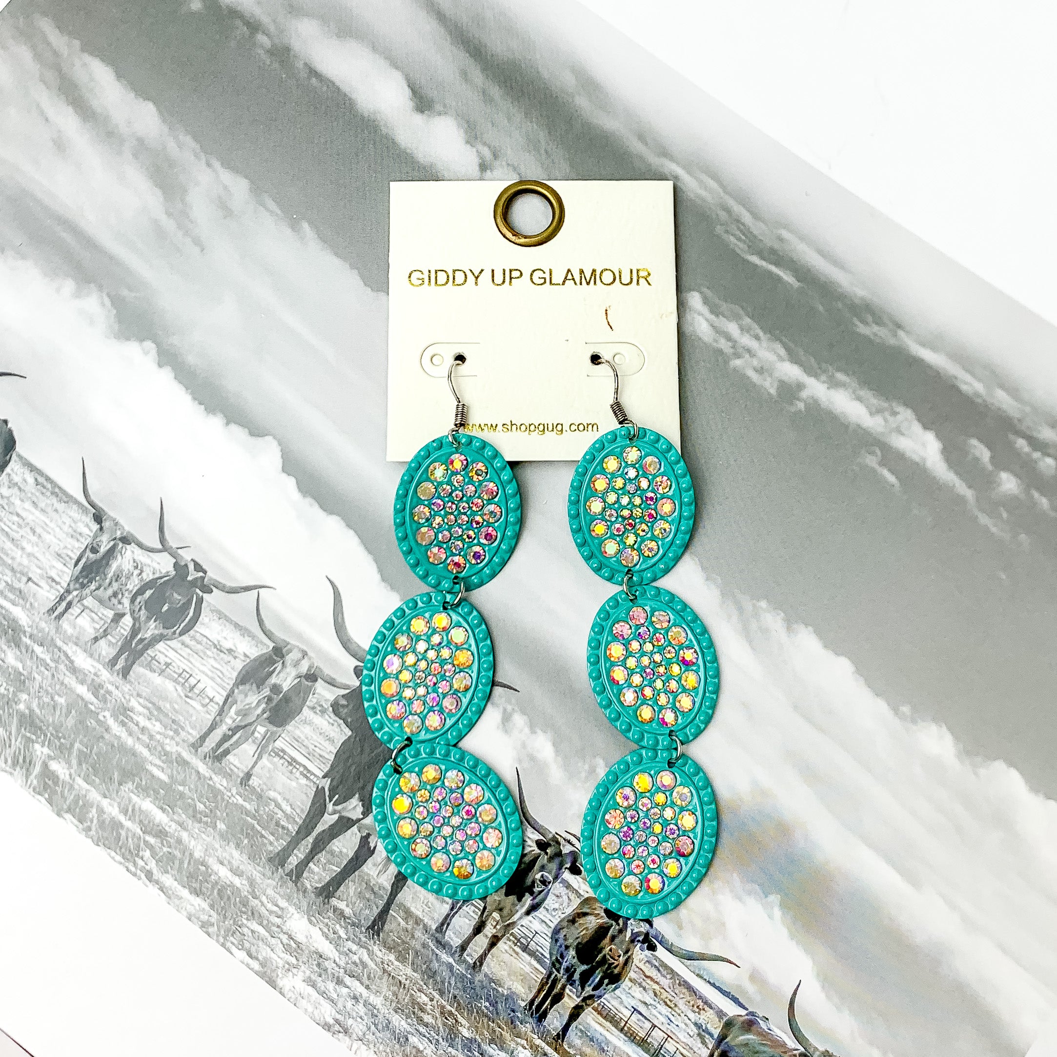 Three tier turquoise oval shape dangle earrings with ab crystals. Pictured on a black and white western picture.