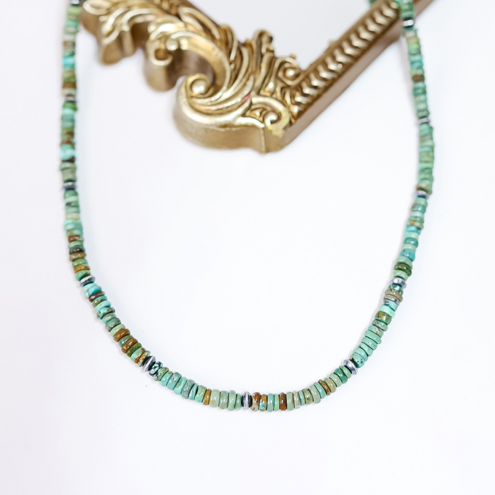 Handmade Red River Turquoise necklace with sterling silver saucer Navajo pearls on white background with ornate gold frame.