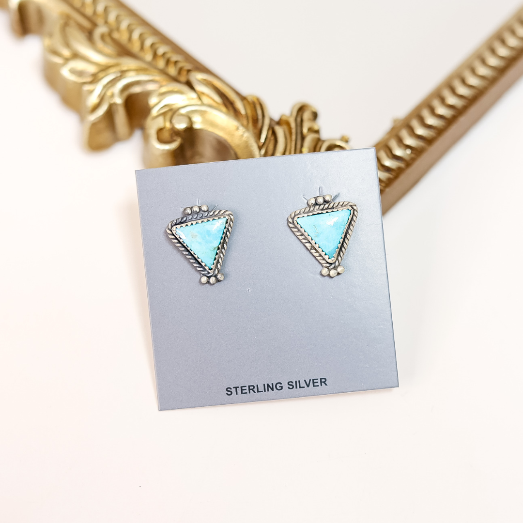 Pair of turquoise triangle earrings on a gray card with 'Sterling Silver' text, against a gold decorative frame background.