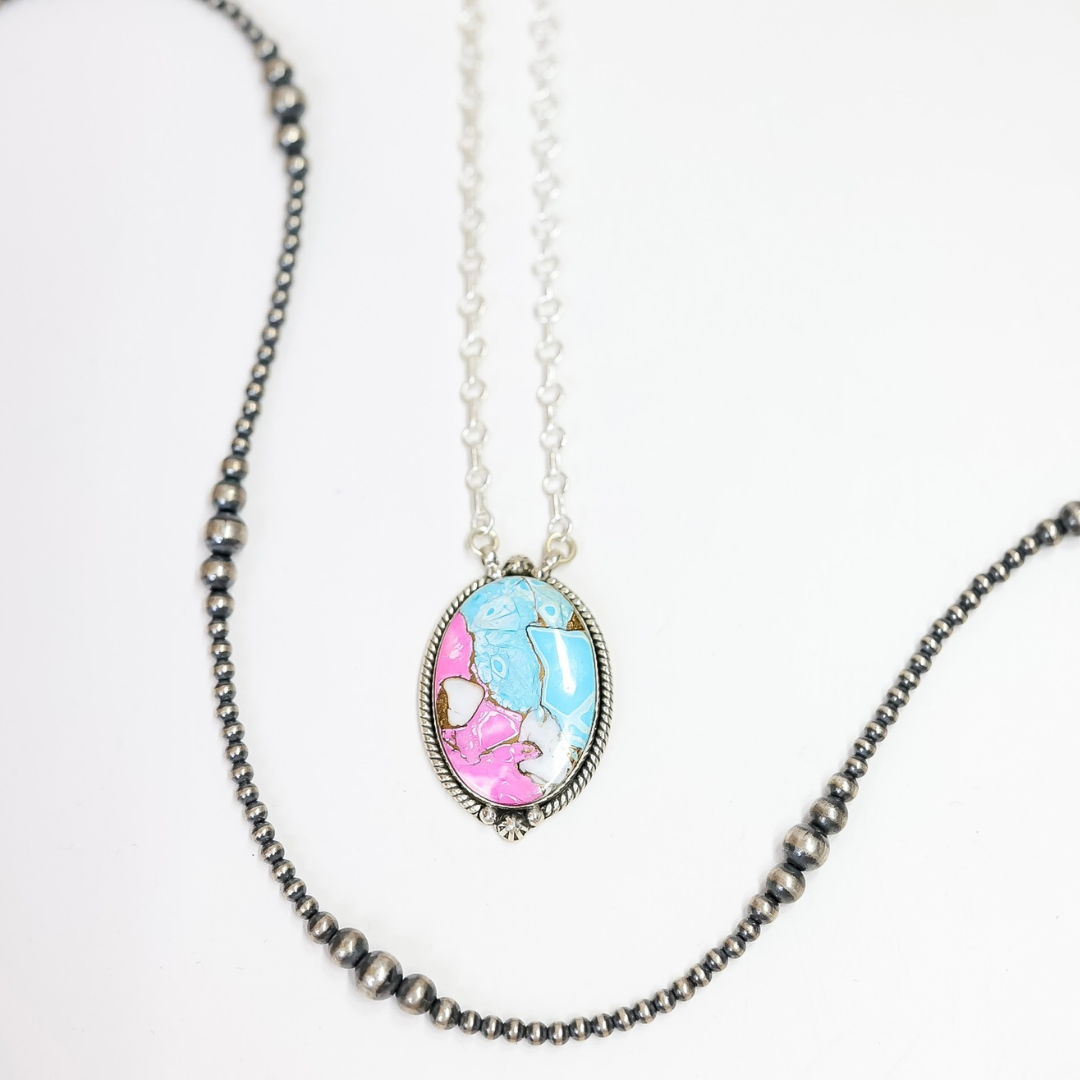 Close-up of a handmade oval necklace featuring hot pink and turquoise stone inlay with sterling silver rope detailing on an adjustable 20-inch chain.