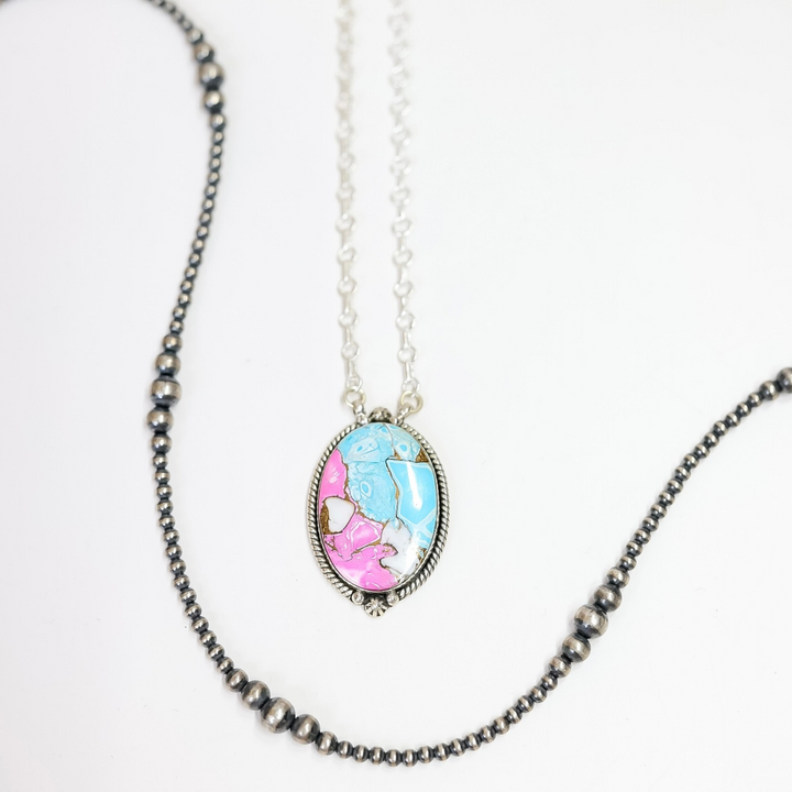 Close-up of a handmade oval necklace featuring hot pink and turquoise stone inlay with sterling silver rope detailing on an adjustable 20-inch chain.