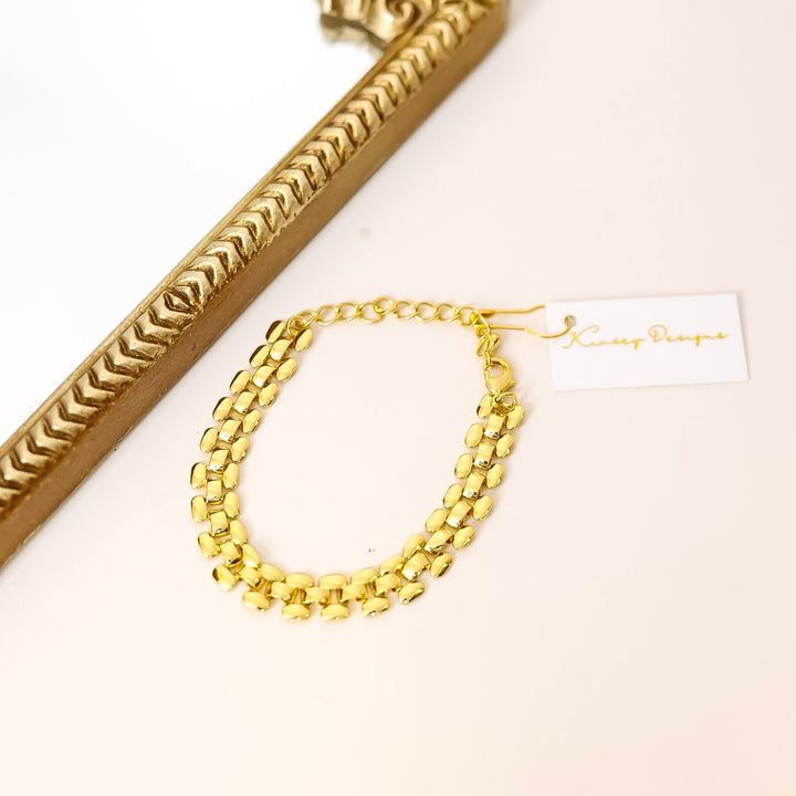 Gold bracelet on a white surface with a decorative gold frame.