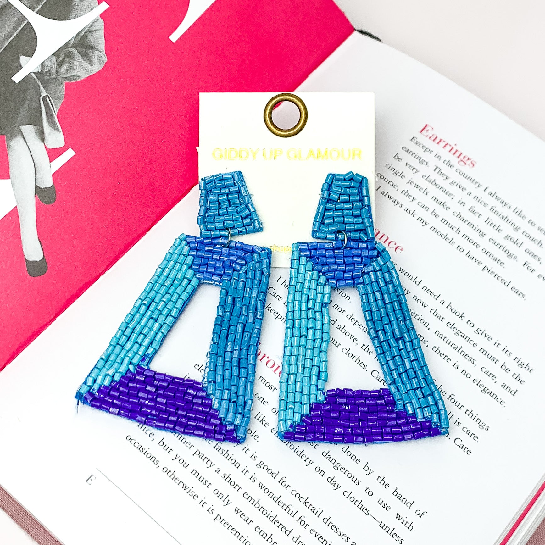Beaded Rectangle Designed Earrings in Shades of Blue. Pictured on a white background with an open book behind the earrings. 