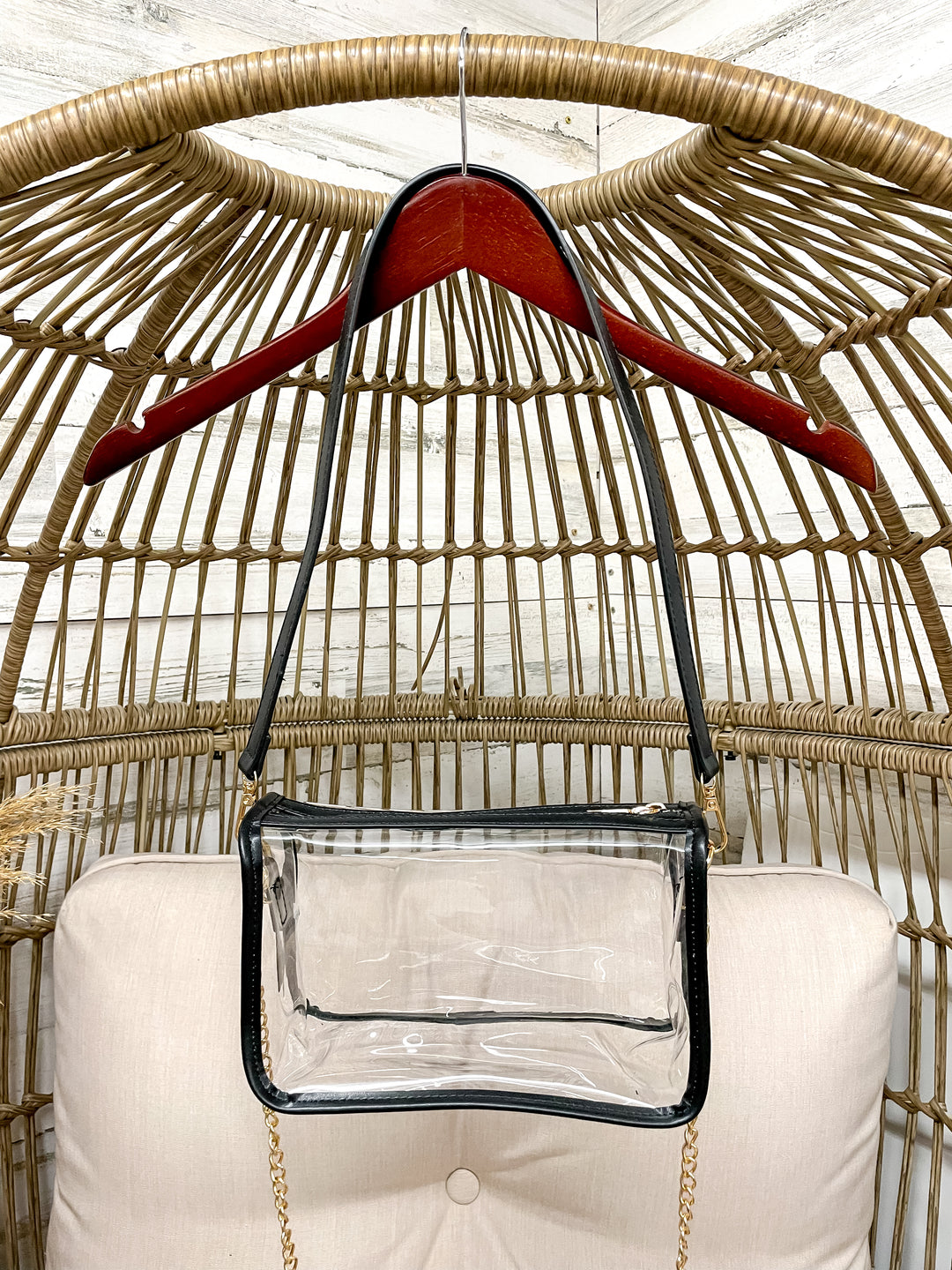 Clear handbag with a red handle hanging on a wicker chair.