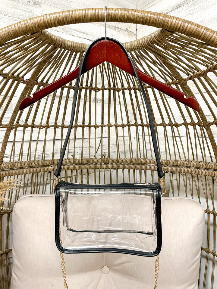 Clear handbag with a red handle hanging on a wicker chair.
