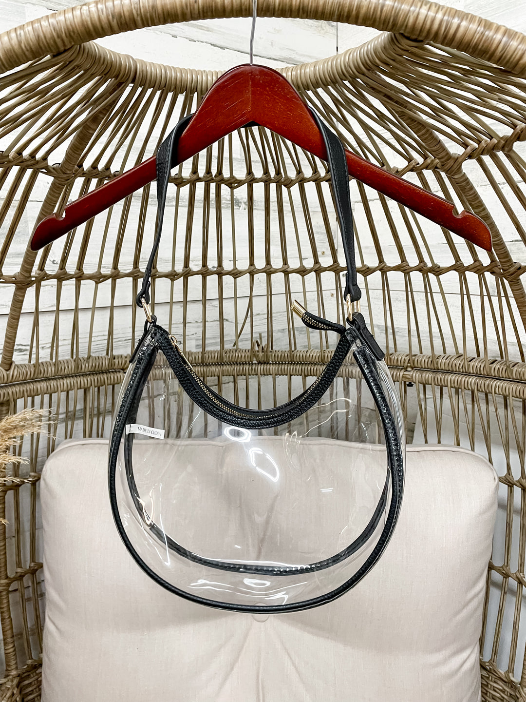 Clear handbag with black handle hanging on a red hanger against a wicker chair background