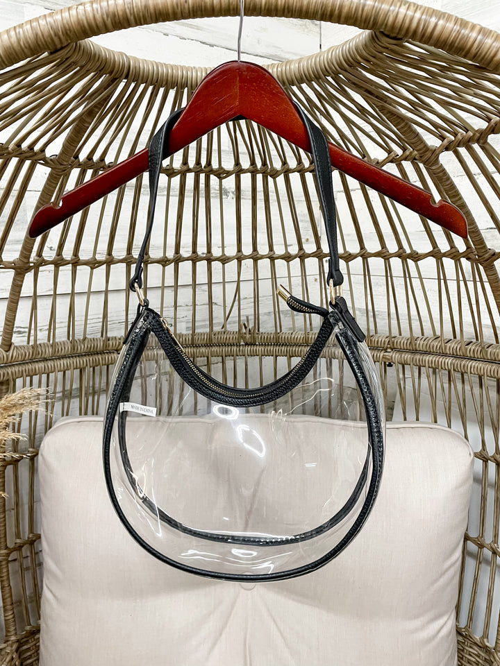 Clear handbag with black handle hanging on a red hanger against a wicker chair background