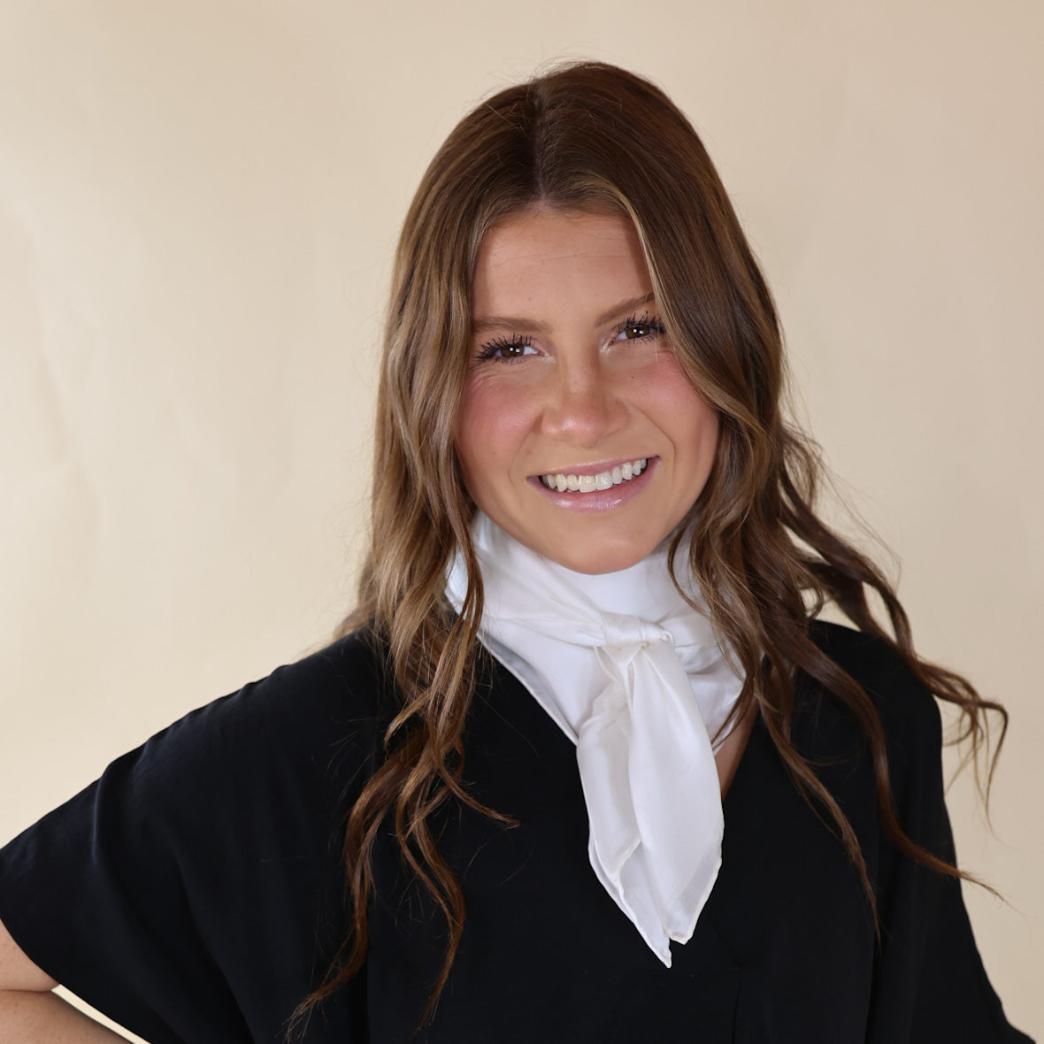 Brunette model is pictured wearing a Black, Drop shoulder top with a Solid White scarf tied around her neck. Model is pictured in front of a beige background. 
