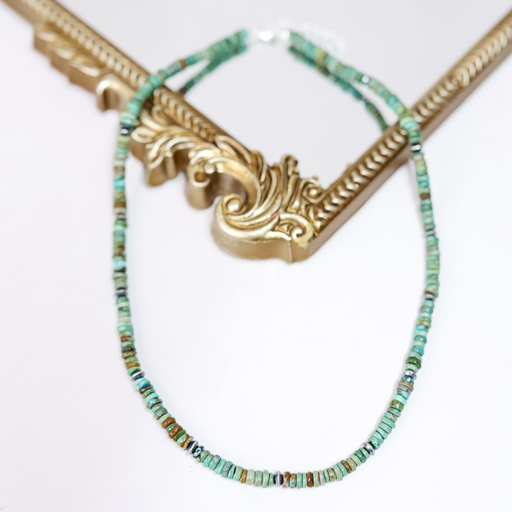 Handmade Red River Turquoise necklace with sterling silver saucer Navajo pearls on white background with ornate gold frame.