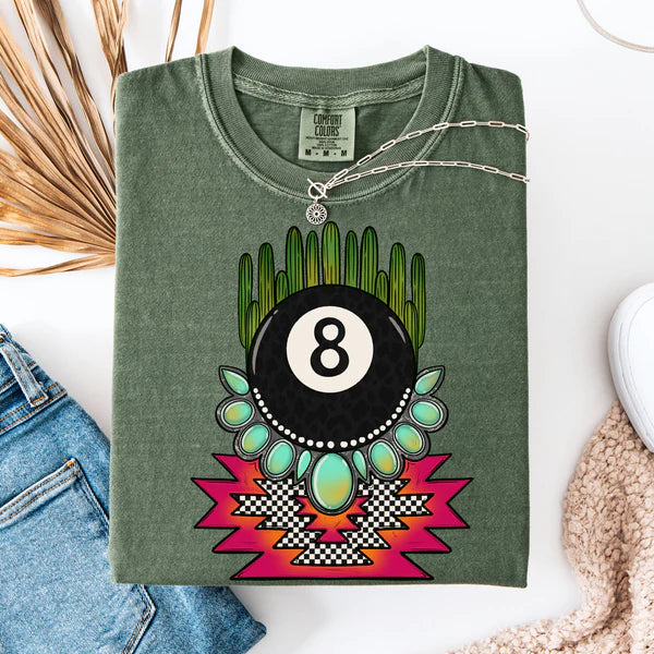 Green t-shirt with a colorful design featuring an eight-ball and cactus, displayed with jeans and a necklace.