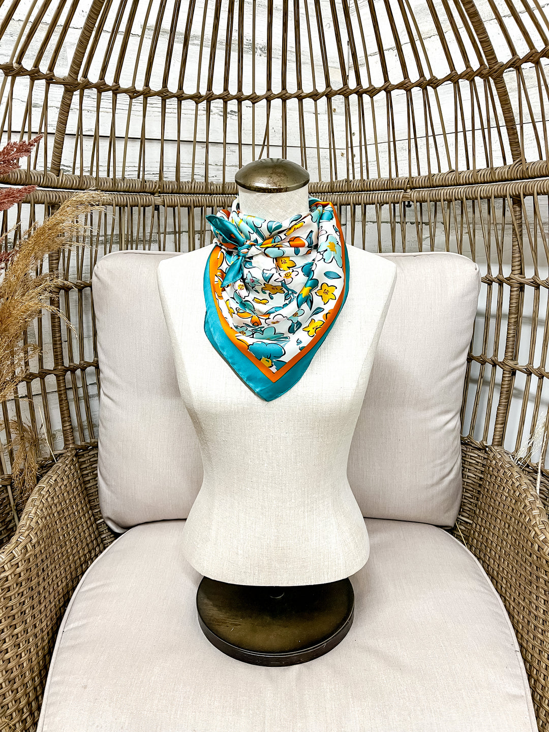 Mannequin head with a colorful scarf draped over it, sitting on a white cushioned chair with a wicker backrest.