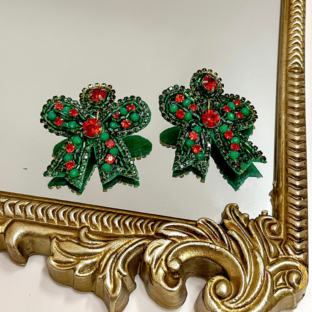 Green and red bow-shaped earrings on a decorative gold mirror