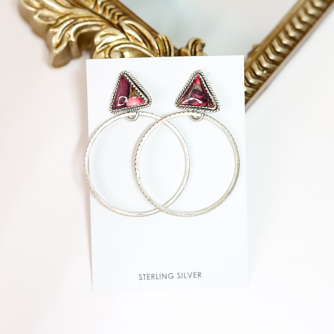 Silver hoop earrings with red gemstones on a white card, gold frame in background
