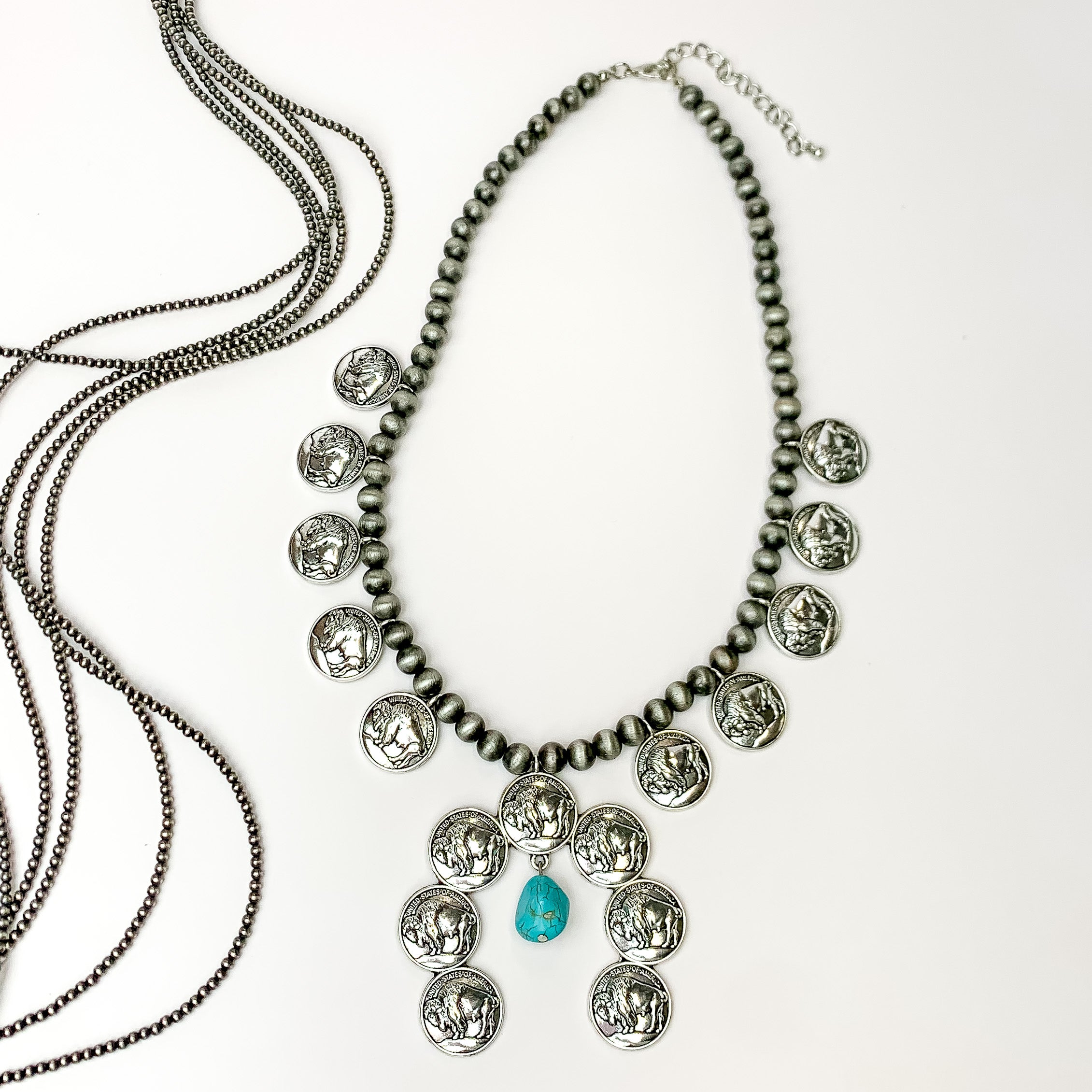 Faux Navajo pearl necklace with buffalo coins around it and a faux turquoise stone that dangles. Pictured on a white background with strands of Navajo pearls next to it.