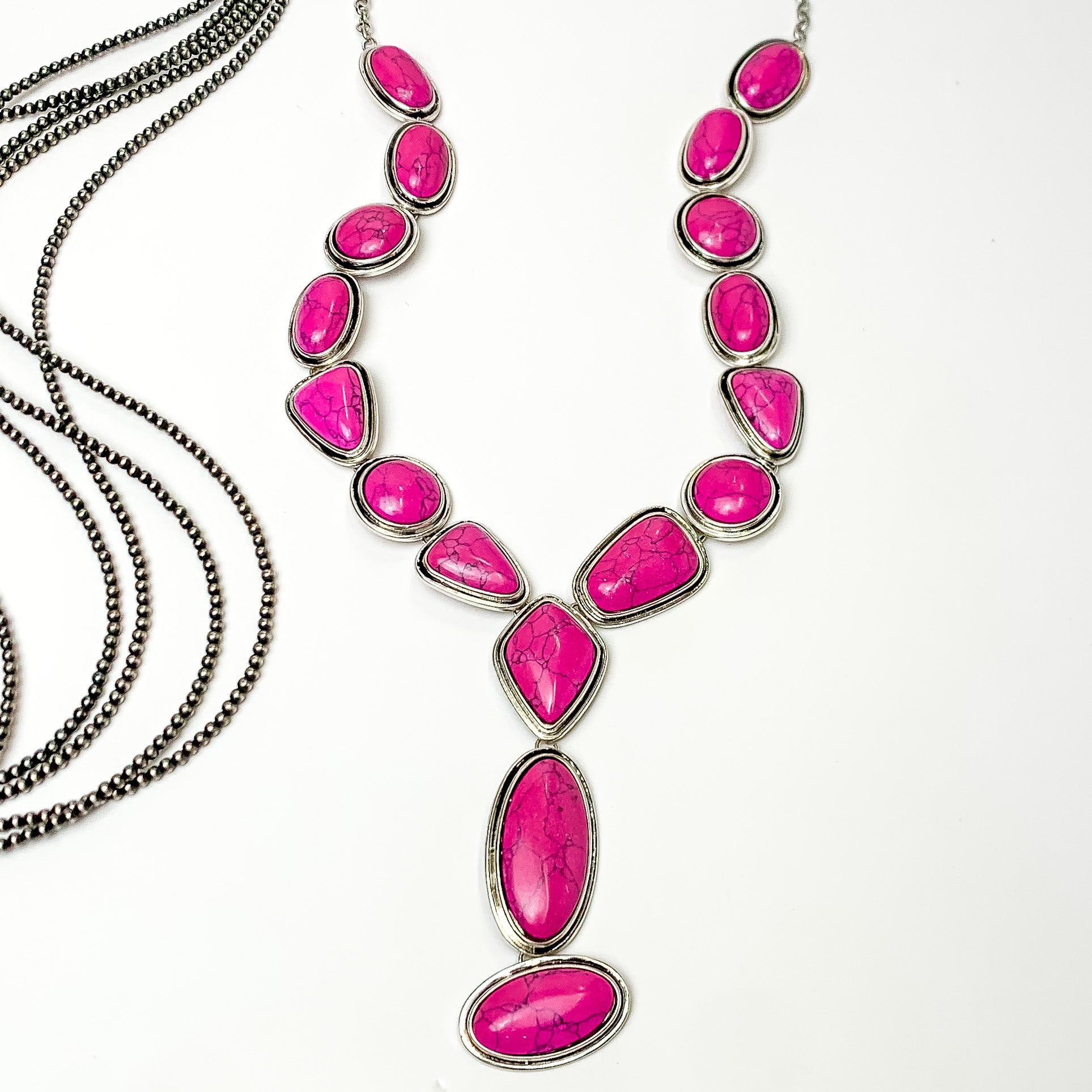 Multi stoned long necklace in pink with a dangling pink stones. Pictured on a white background with Navajo pearl stands.