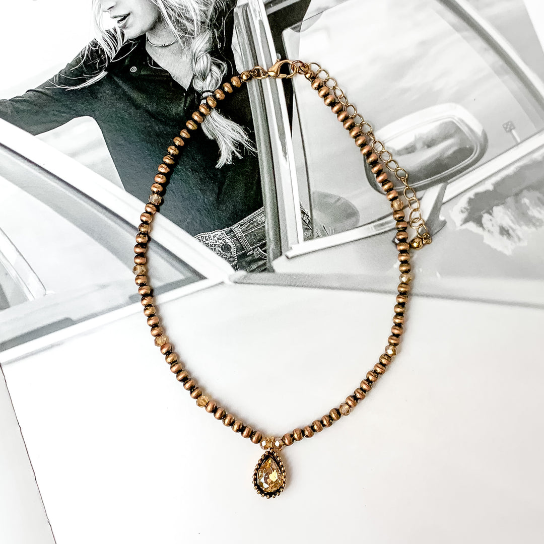 Gold tone short necklace with a crystal drop at the bottom. It does have small crystals through out the gold beads. The background is  a black and white western photo.