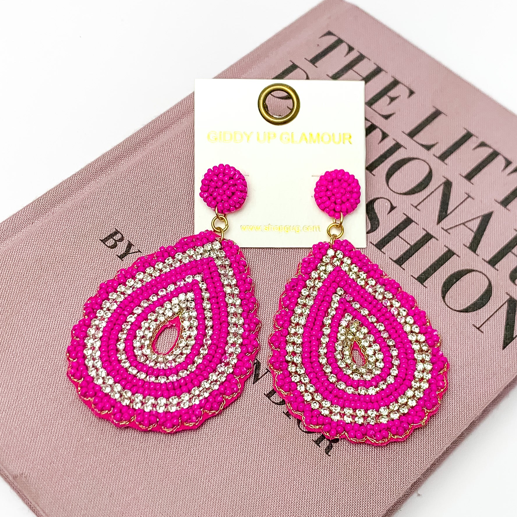 Sound Wave Beaded Drop Earrings with Clear Crystals in Fuchsia. Pictured on a white background with a book behind it.