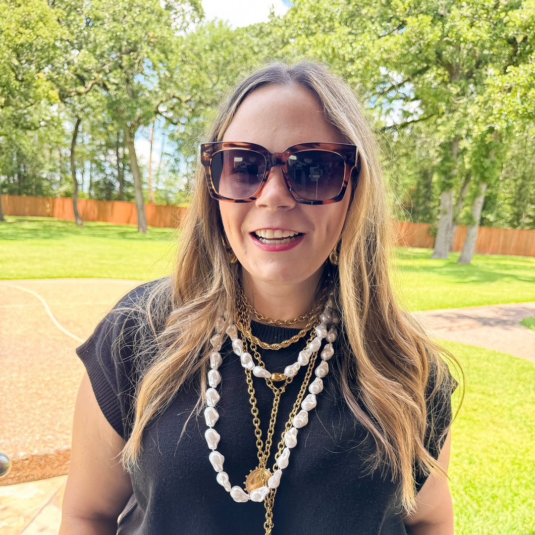 Woman wearing sunglasses and layered necklaces outdoors