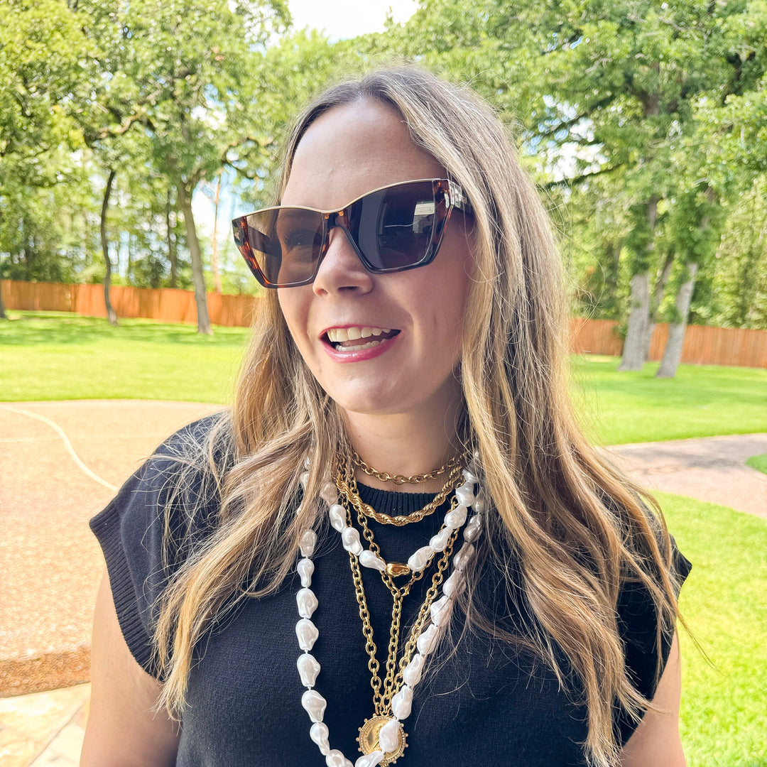 Woman wearing sunglasses and layered necklaces outdoors