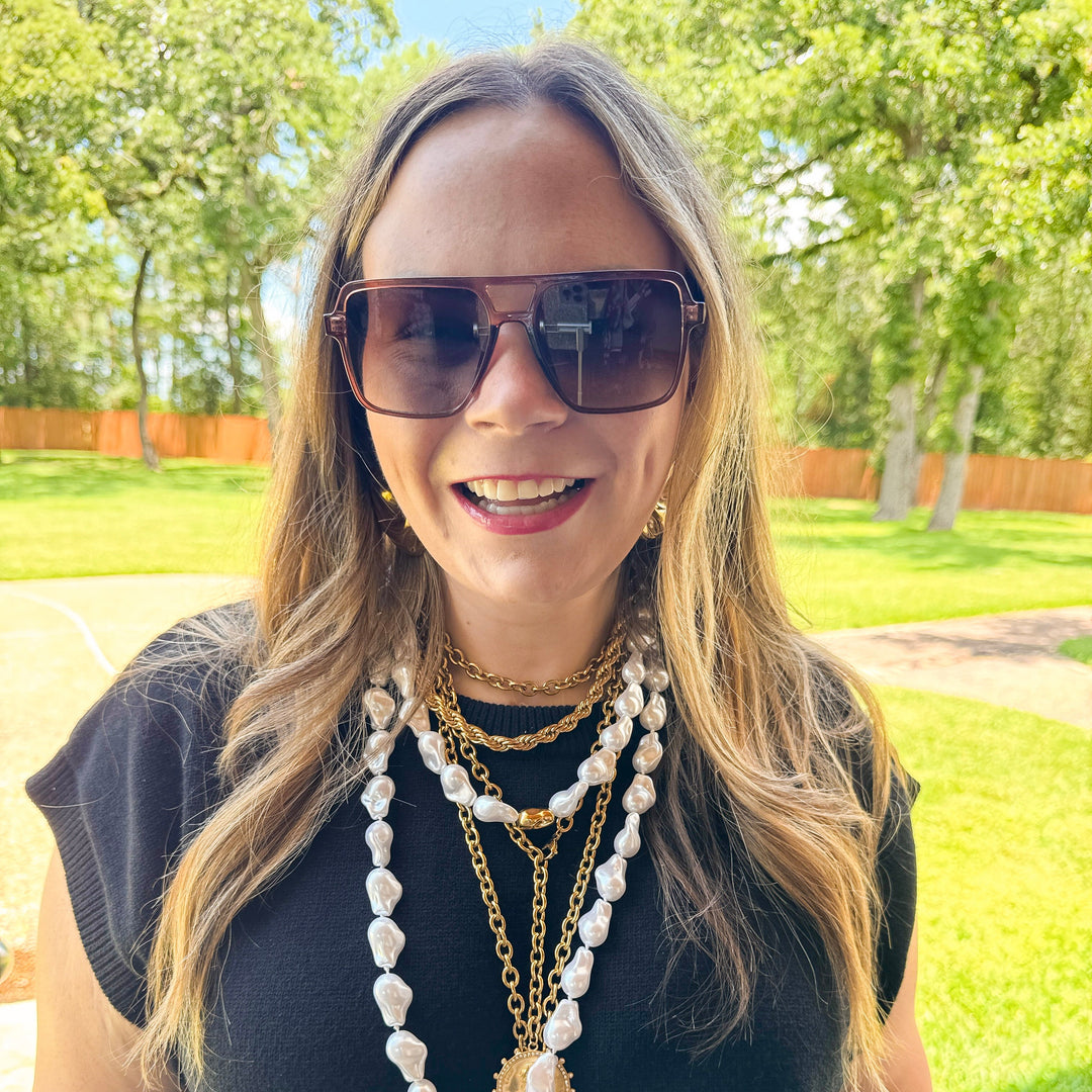 Woman wearing sunglasses and multiple necklaces outdoors